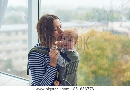 Mother With Ergobaby Carrying Toddler At Home.