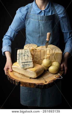 Rustic Gourmet Italian Cheese On Wooden Board In Hands Of Cheese Maker On Black Background