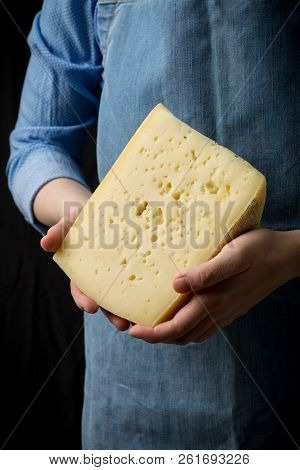 Woman Holding Slice Of Cheese Wearing Blue Apron On Dark Background