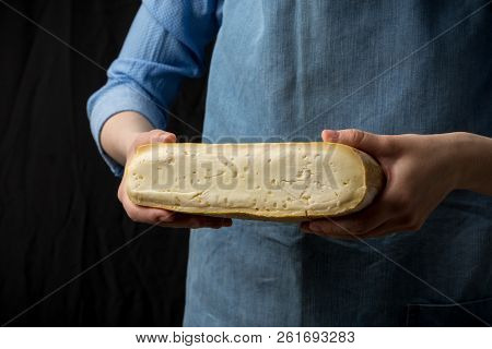 Woman In Blue Apron Holding Taleggio Cheese On Dark Background