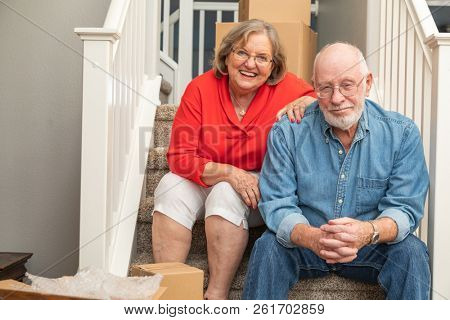 Senior Couple Resting On Stairs Surrounded By Moving Boxes.