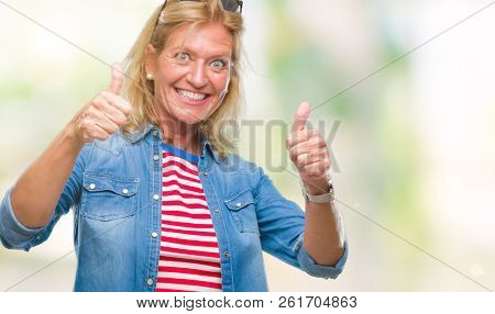 Middle age blonde woman over isolated background approving doing positive gesture with hand, thumbs up smiling and happy for success. Looking at the camera, winner gesture.