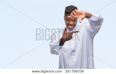 Young arabic african man wearing traditional djellaba over isolated background smiling making frame with hands and fingers with happy face. Creativity and photography concept.