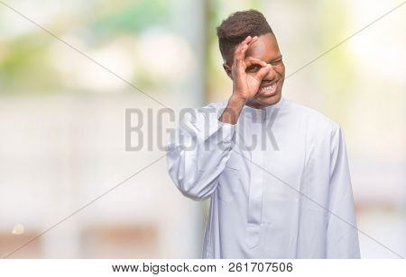 Young arabic african man wearing traditional djellaba over isolated background doing ok gesture with hand smiling, eye looking through fingers with happy face.