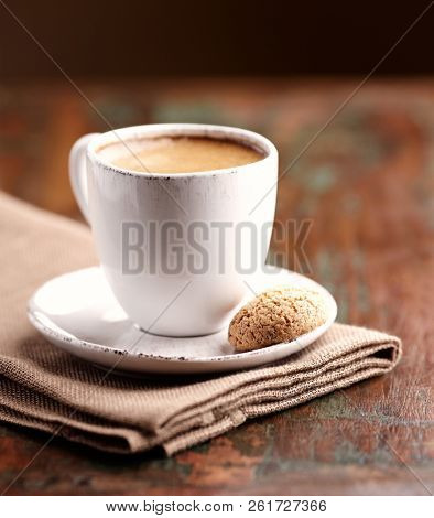 Cup of coffee and biscotti (focus on the biscotti). Brown wooden background. Close up. 