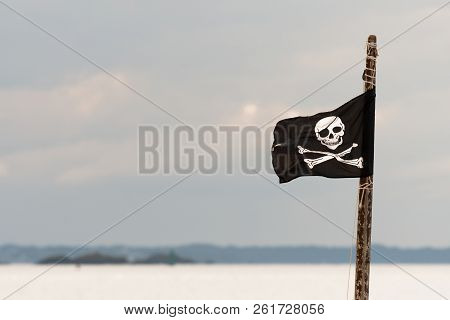 Small Jolly Roger On A Wooden Pole In Front Of Cloudy Sky