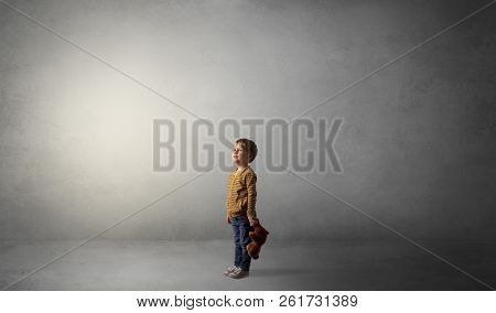 Little waggish kid staying alone in a big empty room with his plush