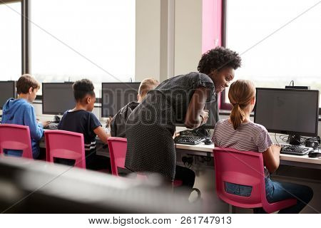 Female Teacher Supervising Line Of High School Students Working at Screens In Computer Class