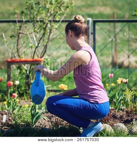 Young Caucasian Girl Watering Flowers With Water Can On A Croft. Side View.