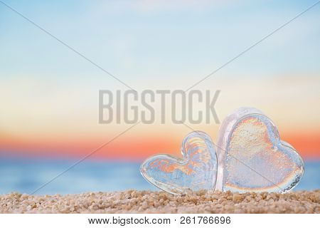 clear heart sea glass  on  beach sand   with bright sunrise or sunset background