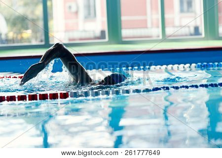 Image of sportive man in blue cap floating in pool in training