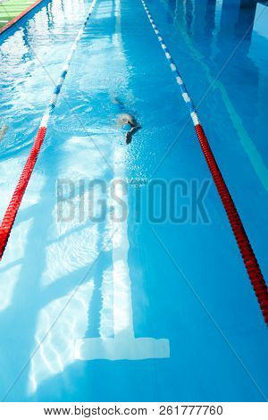 Photo of young athlete man in blue cap swimming on back in swimming pool