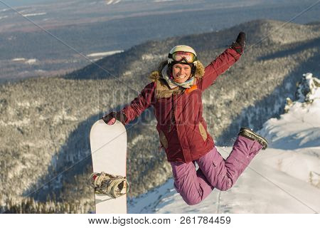 Snowboarder Girl Freerider Is Jump In The Snowy Mountains In Winter Under The Clouds