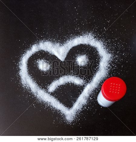 Salt Scattered On Black Surface. Drawn Heart With A Sad Face. Concept- Diet, Harm To Health From Exc