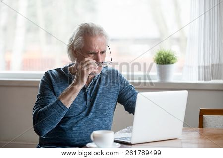 Shocked Frustrated Senior Man Taking Off Glasses Looking At Lapt