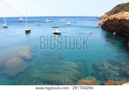 Several Boats Sail Through Crystal Waters Close To Beautiful Village And Beach Of Sa Riera, Mediterr