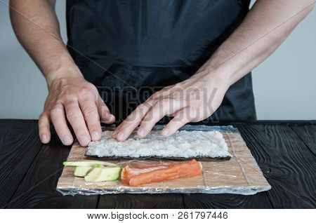 Process of making maki sushi. Cook chef hands preparing rolls with cheese, avocado and sesame seeds