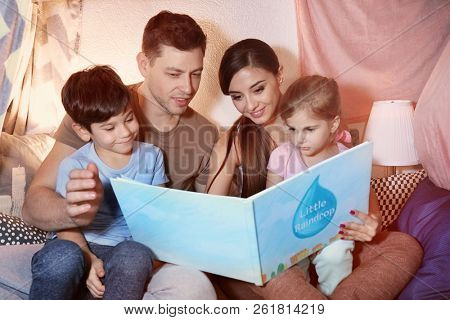 Parents with little children reading  bedtime story in hovel at home