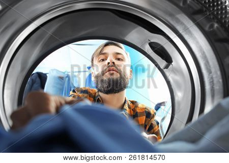 Man doing laundry in laundromat, view from the inside of washing machine