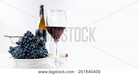 Glass Of Red Wine With A Bottle And A Cluster Of Black Grapes On White Table. Selecive Focus. Copy S