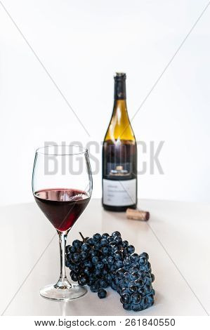 Glass Of Red Wine With A Bottle And A Cluster Of Black Grapes On White Table. Selecive Focus.