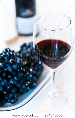 Glass Of Red Wine With A Bottle And A Cluster Of Black Grapes On White Table. Selecive Focus.