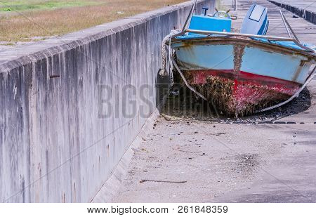 Front View Of Old Dilapidated Red, White And Blue Fishing Boat And Motor With Barnacles On Bottom Si