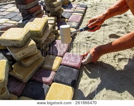 A Worker In The Process Of Laying Multi-colored Paving Slabs. A Man Installs Paving Bricks On A Sand