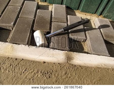 White Rubber Mallet Close Up And Unfinished Work On Laying Gray Paving Slabs 'brick'. Cement-fixed C