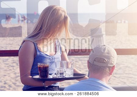 The Waitress Is Carrying Drink To The Client Of In A Cafe On The Beach. Waitress Serving A Client In