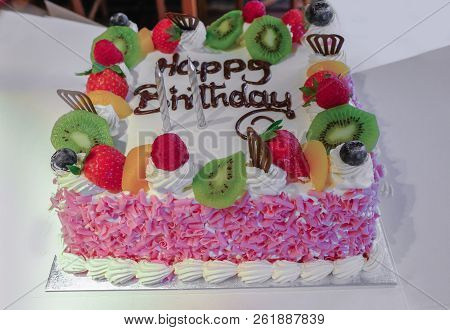 Cream Birthday Cake With Fresh Fruit On The Top And Pink Flakes Decorating The Sides.  Happy Birthda