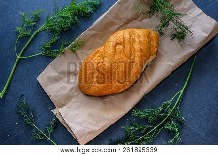 A Loaf Of White Bread On Brown Kraft Paper, Surrounded By Dill On A Dark Background.