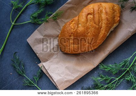 A Loaf Of White Bread On Brown Kraft Paper, Surrounded By Dill On A Dark Background.