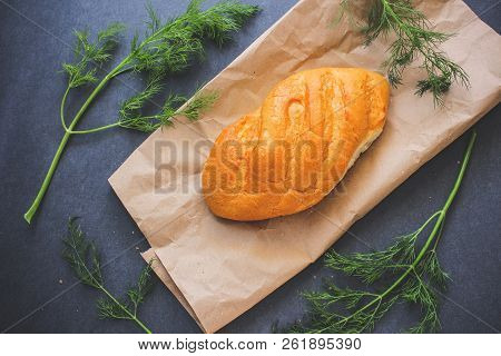 A Loaf Of White Bread On Brown Kraft Paper, Surrounded By Dill On A Dark Background.