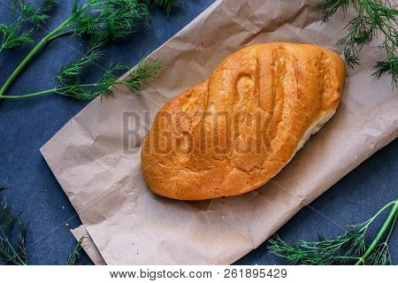 A Loaf Of White Bread On Brown Kraft Paper, Surrounded By Dill On A Dark Background.