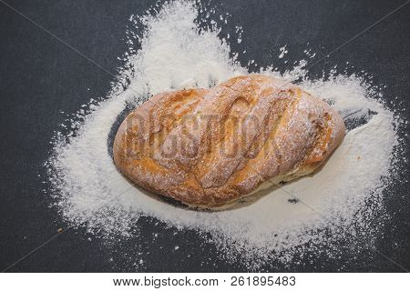 A Loaf Of White Bread On Dark Kraft Paper, Powdered With Flour.
