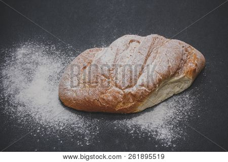 A Loaf Of White Bread On Dark Kraft Paper, Powdered With Flour.