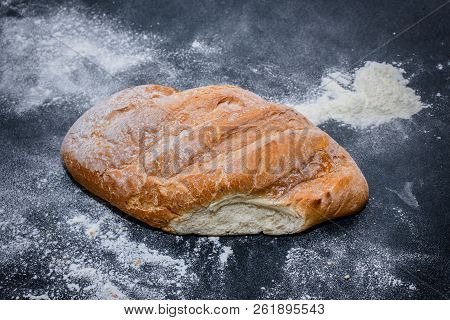 A Loaf Of White Bread On Dark Kraft Paper, Powdered With Flour.
