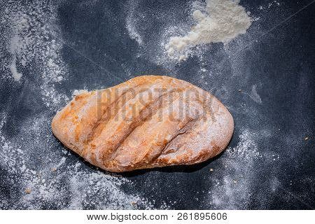 A Loaf Of White Bread On Dark Kraft Paper, Powdered With Flour.