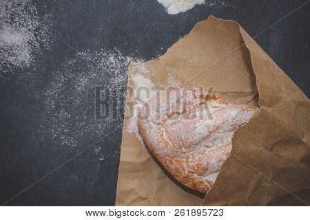 A Loaf Of White Bread On Brown Craft Paper, Powdered With Flour On A Dark Table Background.