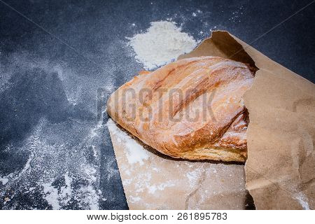A Loaf Of White Bread On Brown Craft Paper, Powdered With Flour On A Dark Table Background.