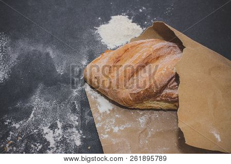 A Loaf Of White Bread On Brown Craft Paper, Powdered With Flour On A Dark Table Background.