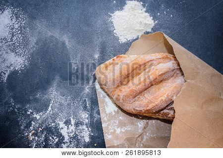 A Loaf Of White Bread On Brown Craft Paper, Powdered With Flour On A Dark Table Background.