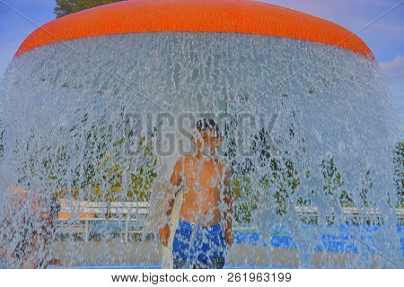 Little Boy In The Small Swimming Pool. Boy Taking Shower In Water Park. Boy Standing Under Sprinkler