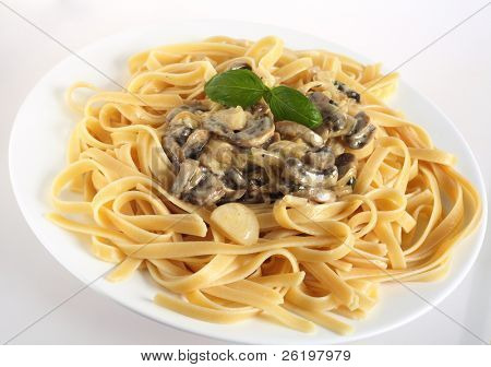Une assiette de fettuccini garni de champignons dans une sauce crème, surmonté d'un brin de basilic