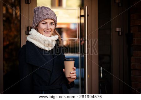 Young Female Student In Warm Autumn Clothes Coming Out Of The House With A Backpack With Books And A