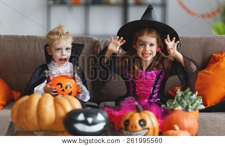 Happy Children In Costumes Of Witch And Vampire  Preparing The Home For Holiday Halloween