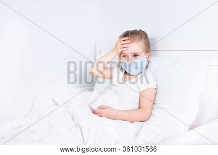 Little Girl In Protective Medical Mask Staying In Bed And Touching Her Head. Headache, Migraine, Fea