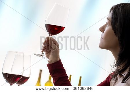 Close Up Portrait Of Female Enologist Evaluating Red Wine. Side View Of Woman Holding Red Wine Glass