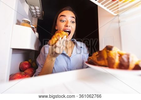 Cheat Meal. Young Woman Taking Plate With Croissants From Fridge, Biting One, View From Inside